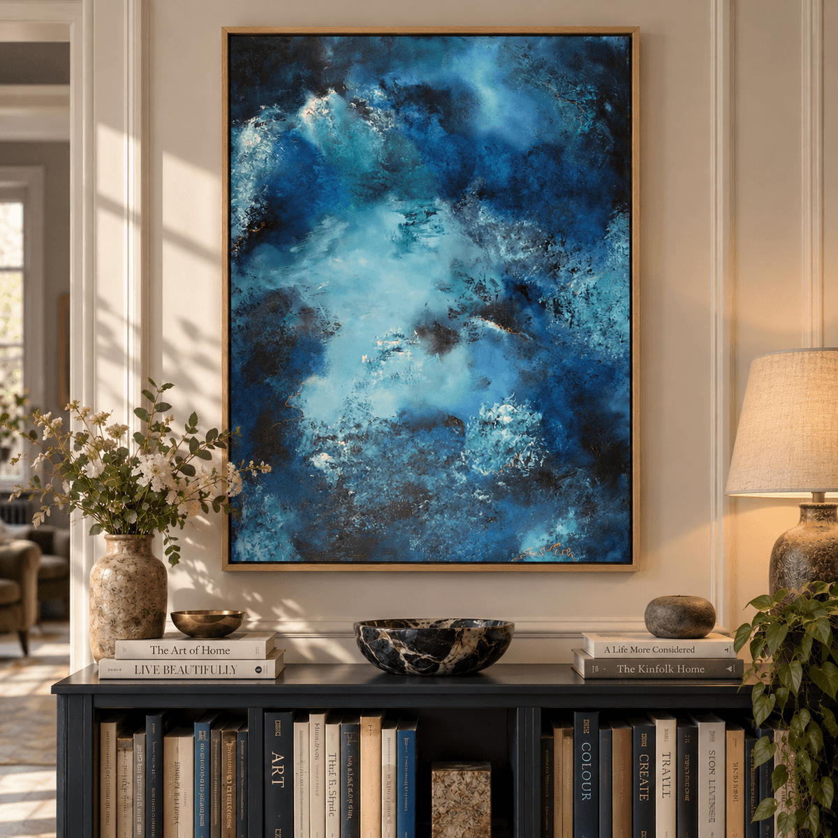 A large framed abstract canvas print featuring swirling shades of blue, teal, and black, displayed on a wall above a dark bookshelf in a styled living room setting.