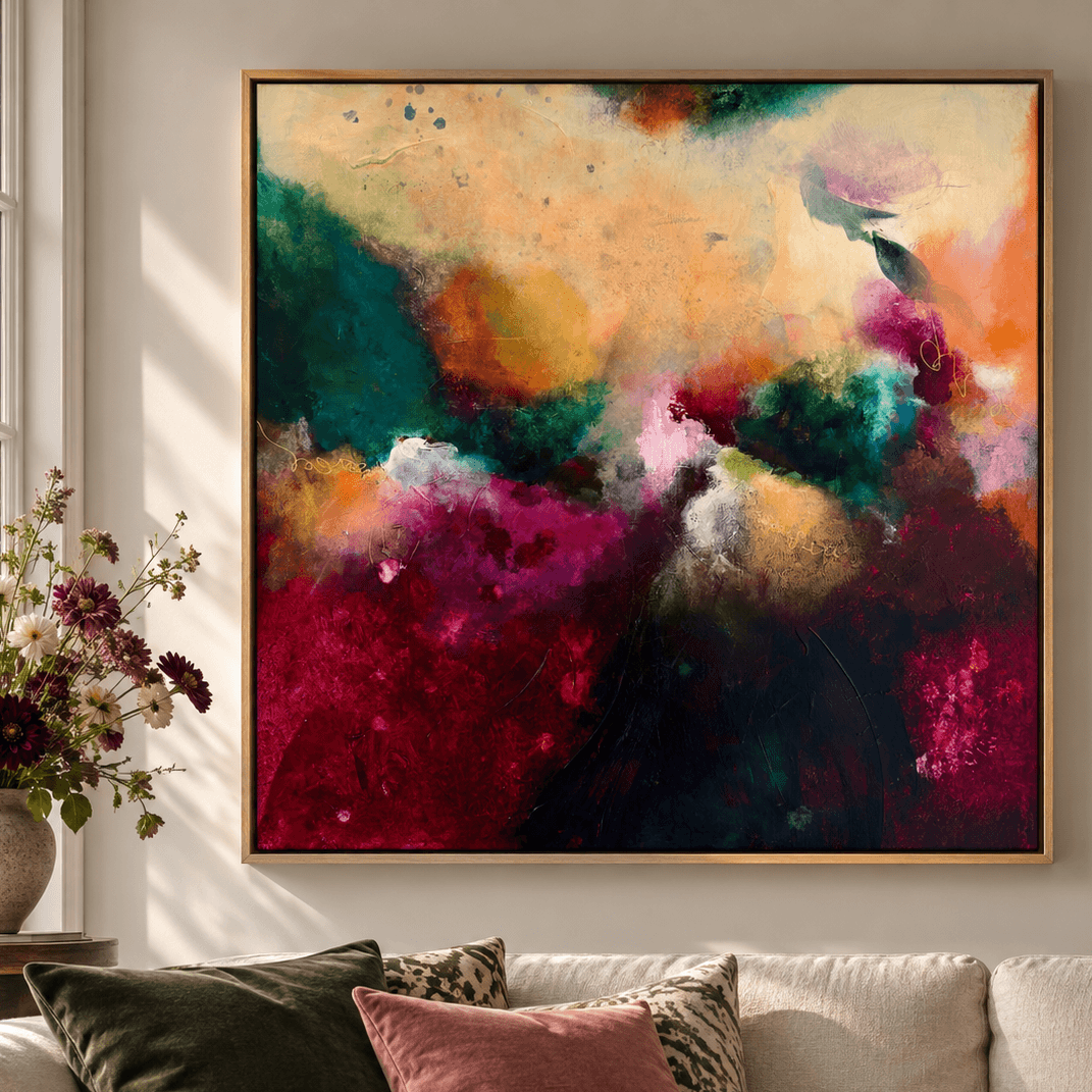 A large framed abstract canvas painting with vibrant splashes of green, teal, magenta, orange, and cream, hanging on a light beige wall above a modern white sofa with green and pink pillows.